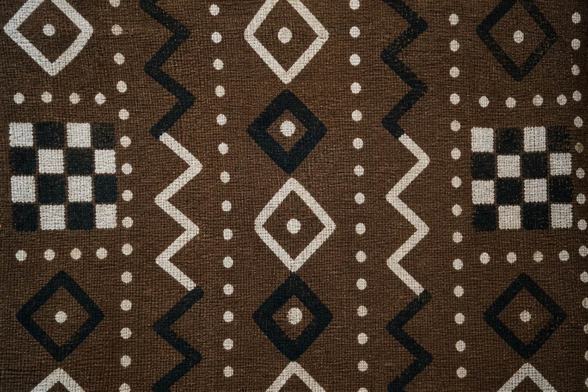 Détail de motifs géométriques blancs et noirs peints à la main sur coton brun, trame irrégulière visible de près