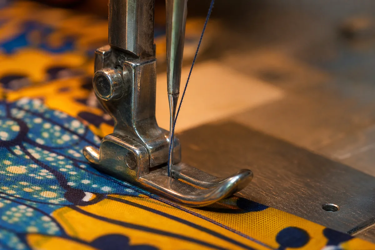 Gros plan sur le pied-de-biche d’une machine à coudre et un tissu wax coloré