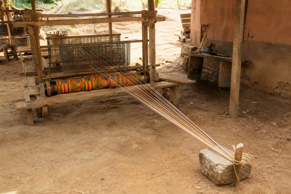 Métier à tisser horizontal en bois dans un atelier ghanéen, bande de tissu coloré tendue vers un poids