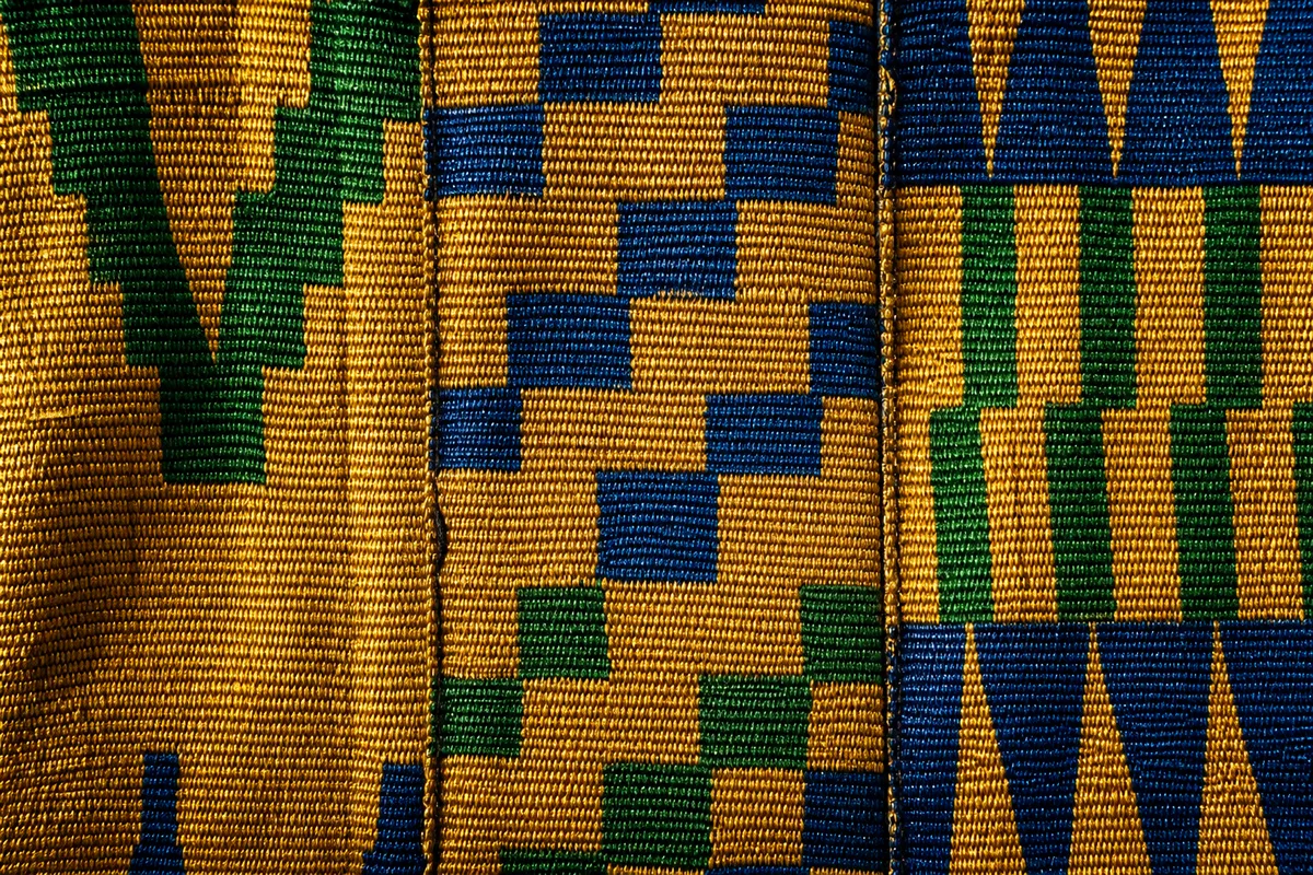 Détail de bandes de kente cousues bord à bord, motifs géométriques or, vert et bleu en lumière rasante